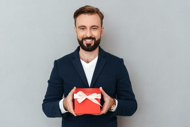 Улыбающийся бородатый мужчина в деловой одежде держит подарок