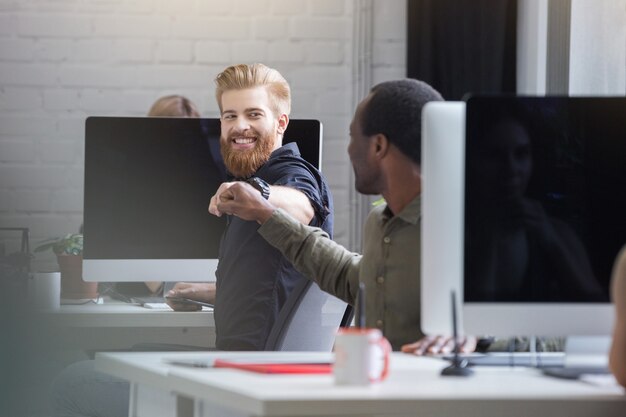 男性の同僚に拳バンプを与えるひげを生やした男の笑みを浮かべてください。