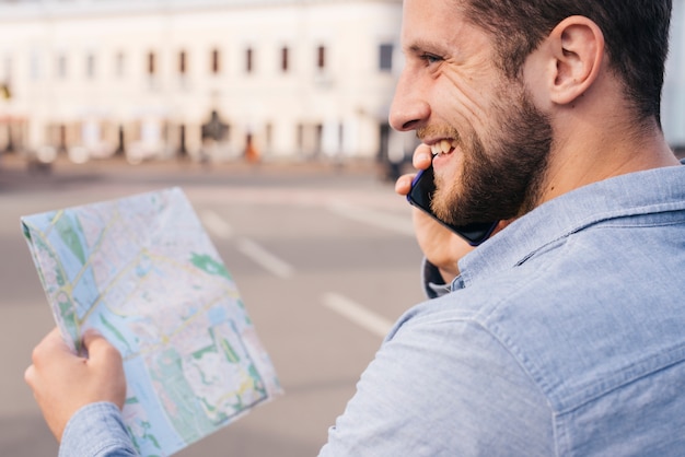 Free photo smiling bearded man holding map while talking on cell phone