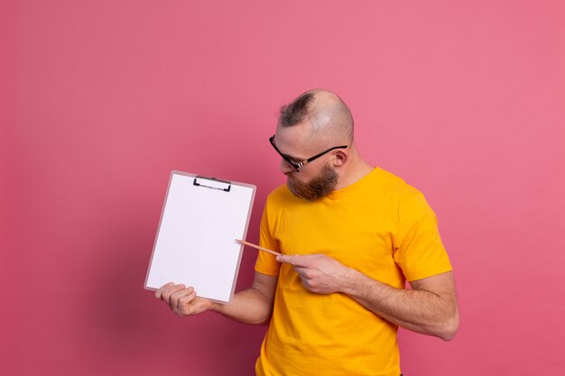 Smiling bearded man wearing eyeglasses wearing casual clothes holding a clipboard with a blank paper pointing