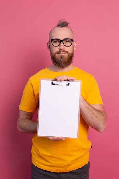 Smiling bearded man wearing eyeglasses wearing casual clothes holding a clipboard with a blank paper pointing