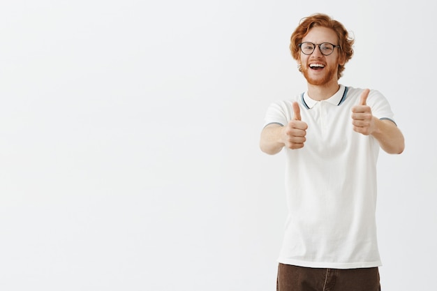 Free photo smiling bearded redhead guy posing against the white wall with glasses