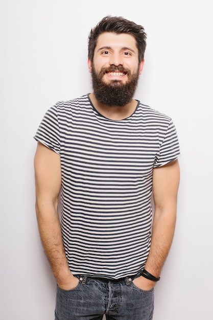 Modello maschio giovane barbuto sorridente vestito casualmente, isolato sopra il muro bianco.