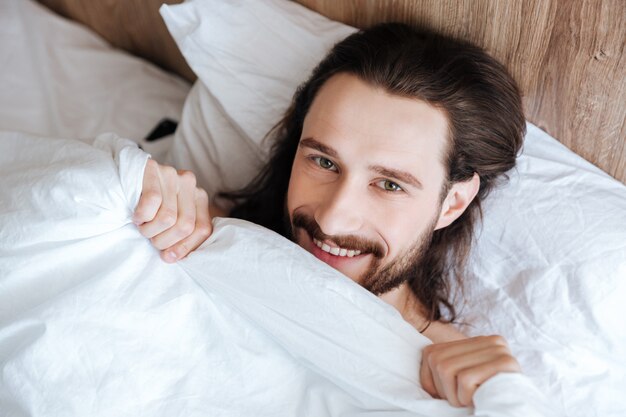 Smiling bearded young man lying in bed