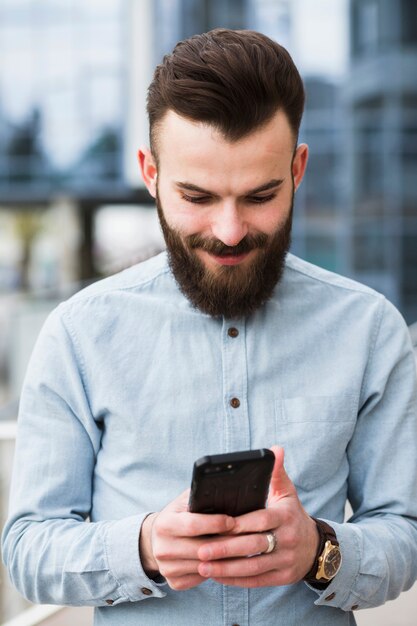 Smiling bearded young man text messaging on mobile phone