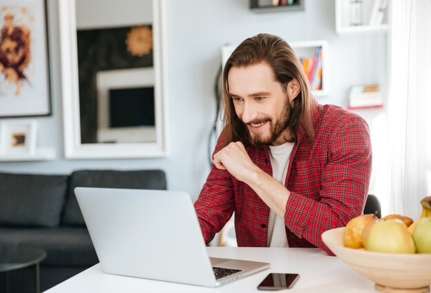 Smiling bearded young man using laptop at home