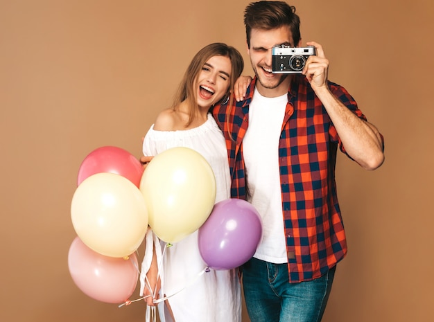 美しい少女とカラフルな風船の束を持って彼女のハンサムなボーイフレンドの笑みを浮かべてください。幸せなカップルは、レトロなカメラで自分の写真を撮る。お誕生日おめでとうございます