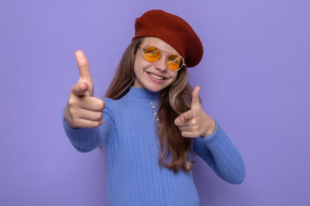 Smiling beautiful little girl pointing at front, wearing hat with glasses