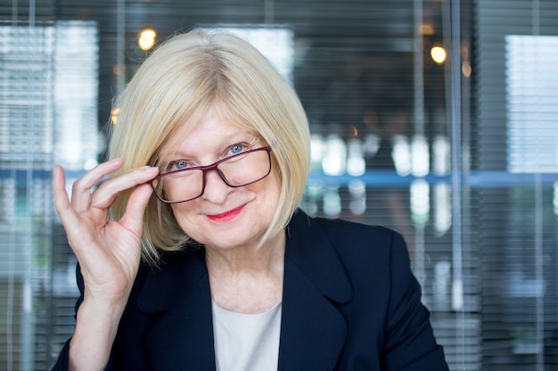 Smiling beautiful senior woman putting glasses on