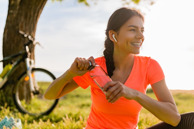 Free Photo smiling beautiful woman drinking water in bottle doing sports in morning in park