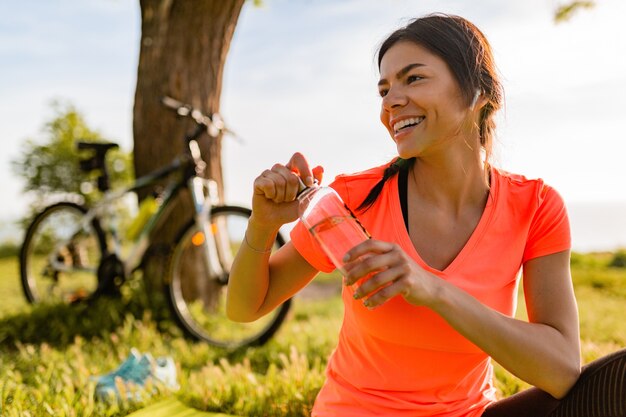 公園で朝のスポーツをしているボトルの水を飲む美しい女性の笑顔