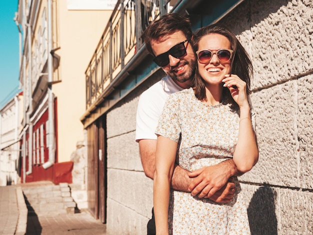 Smiling beautiful woman and her handsome boyfriend Woman in casual summer clothes Happy cheerful family Female having fun Couple posing on the street background in sunglassesHugging each other