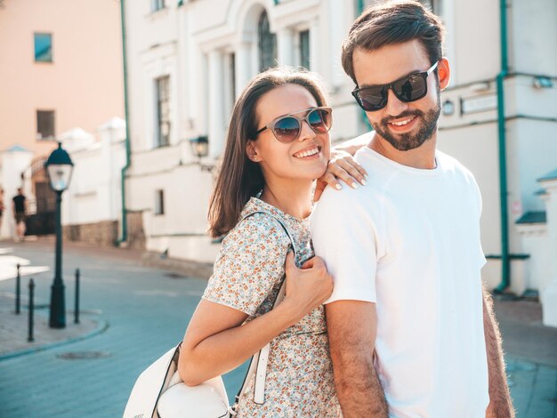 Smiling beautiful woman and her handsome boyfriend Woman in casual summer clothes Happy cheerful family Female having fun Couple posing on the street background in sunglassesHugging each other