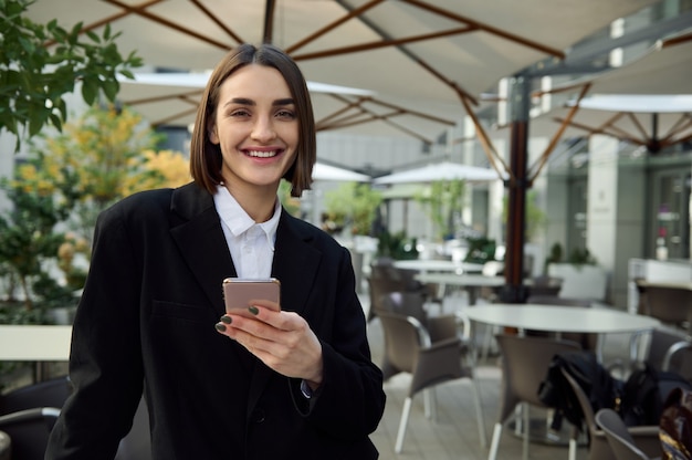 Smiling beautiful woman holding cell phone smartphone, typing text messages, messaging, swiping web page. business, finance, online remote work, online shopping, communication and connection concepts
