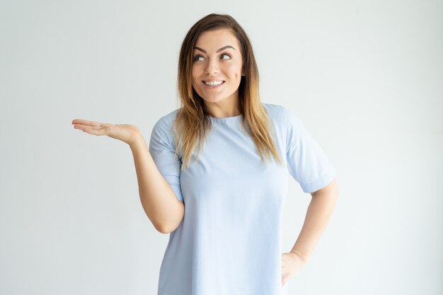 Smiling beautiful woman holding empty space on palm and looking aside.