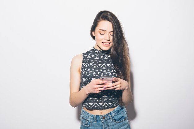 Smiling beautiful woman holding mobile phone isolated on a white wall