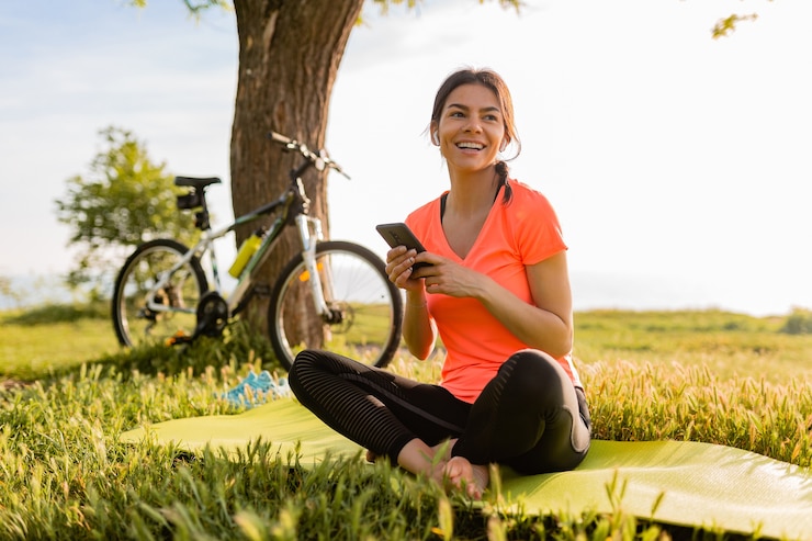 Free Photo smiling beautiful woman holding phone doing sports in morning in park nature