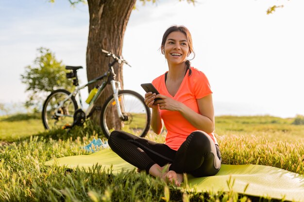 Smiling beautiful woman holding phone doing sports in morning in park nature