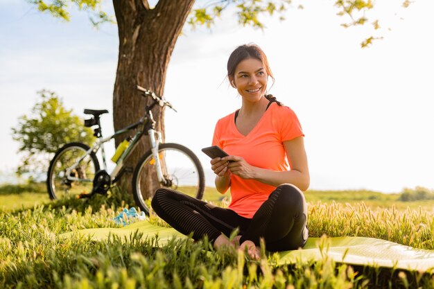 Smiling beautiful woman holding phone doing sports in morning in park