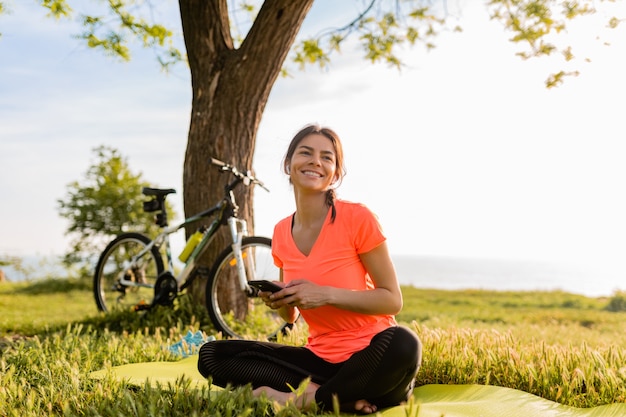 Smiling beautiful woman holding phone doing sports in morning in park