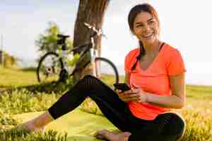 Foto gratuita sorridente bella donna che tiene il telefono facendo sport mattina nel parco