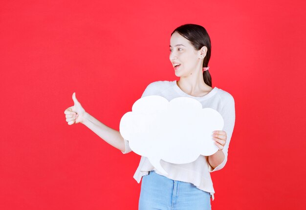 Smiling beautiful woman holding speech bubble and gesturing thumb up