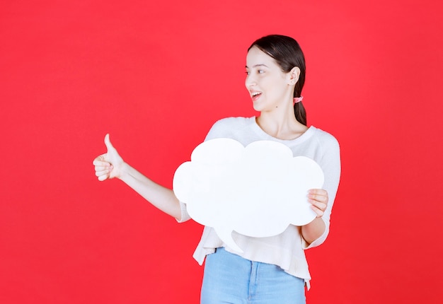 Smiling beautiful woman holding speech bubble and gesturing thumb up