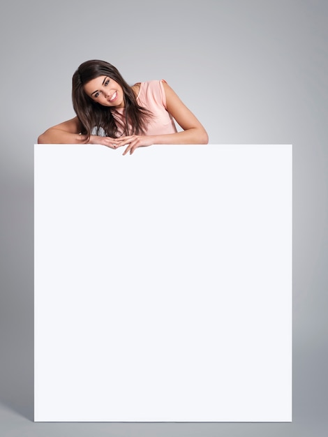 Smiling beautiful woman leaning on empty whiteboard