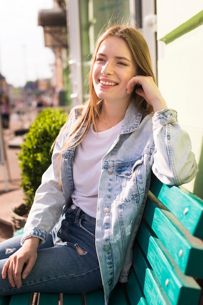 Bella donna sorridente che si siede sul banco all'aperto