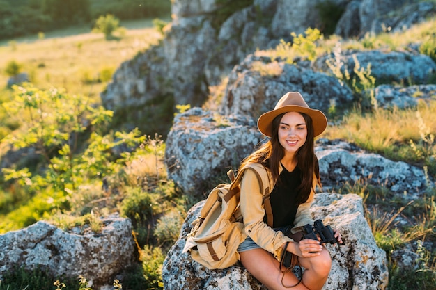 Smiling beautiful woman sitting on rock holding binocular