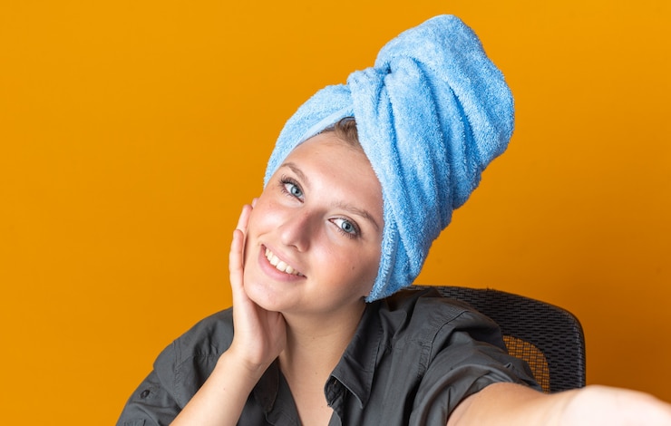 Free Photo smiling beautiful woman wrapped hair in towel taking selfie and putting hand hand on cheek