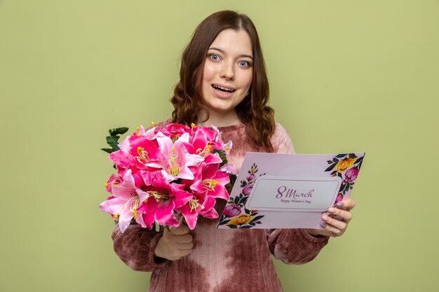 Улыбающаяся красивая молодая девушка в счастливый женский день держит букет с поздравительной открыткой