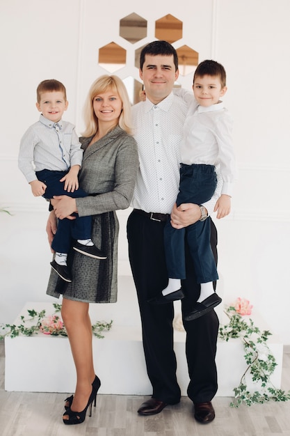 Sorridenti bei giovani genitori e i loro figli che guardano la telecamera mentre posano contro il muro bianco. concetto di famiglia e genitorialità