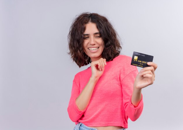 Smiling beautiful young woman holding card on isolated white wall with copy space