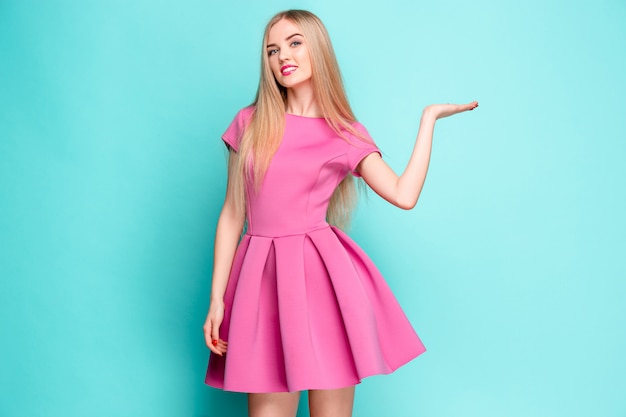 Smiling beautiful young woman in pink mini dress posing, presenting something