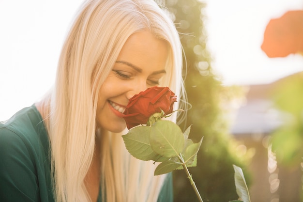 Foto gratuita bella giovane donna sorridente che odora rosa rossa