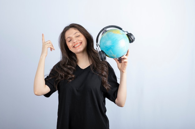 ヘッド​フォン​で​地球儀​を​立って​保持している​美しい​若い​女性​の​笑顔​。