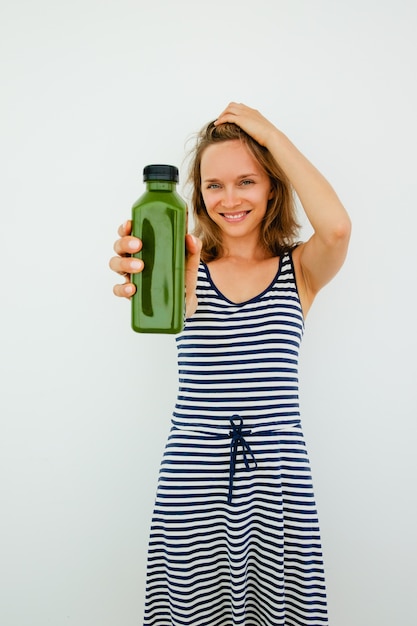 Free photo smiling beautiful young woman using natural shampoo and showing product to camera. happy girl drinking smoothie to be healthy. choice concept