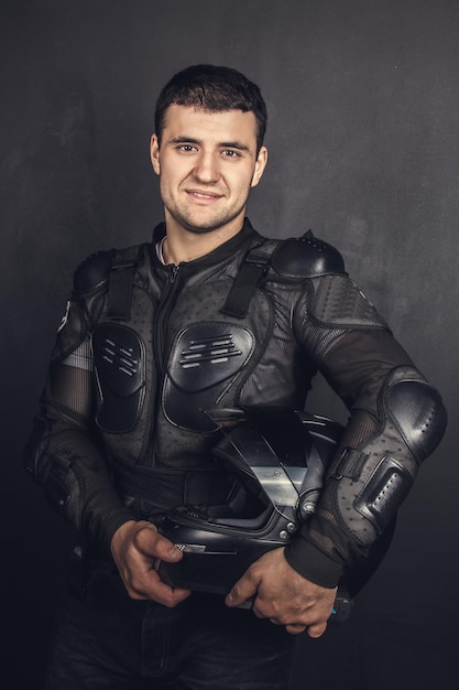 Smiling biker in protection holds black helmet. Isolated on grey background.