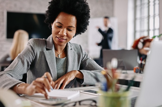 Smiling black entrepreneur working on financial reports at her desk in the office There are people in the background