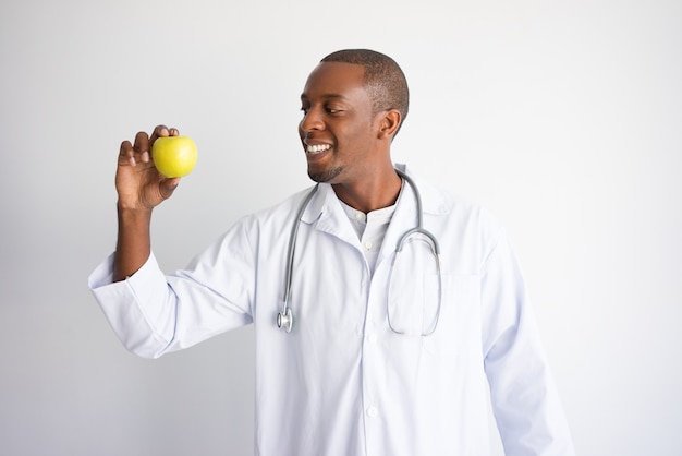 Smiling black male doctor holding green apple. 