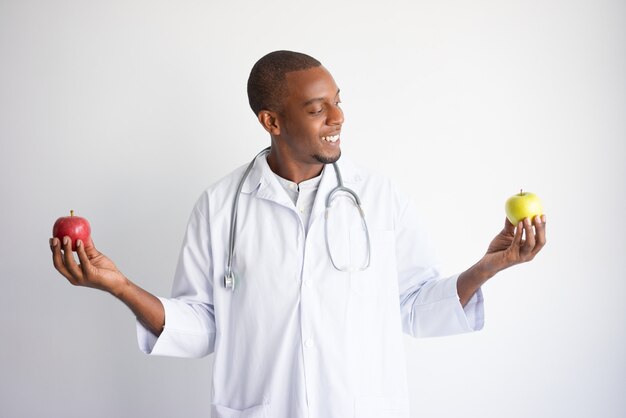 Smiling black male doctor holding green and red apples. 