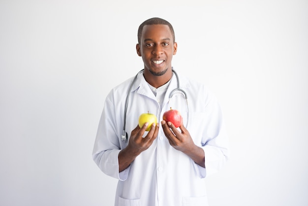 Smiling black male doctor holding yellow and red apple. 