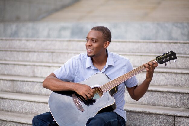 Улыбающийся черный человек, играющий на гитаре и сидящий на лестнице