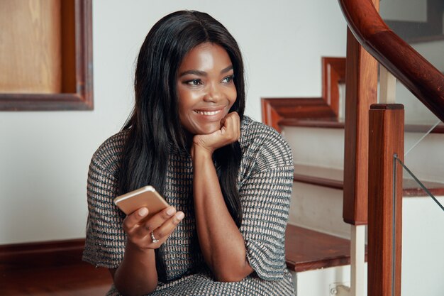 Smiling black woman sitting with phone on stairs