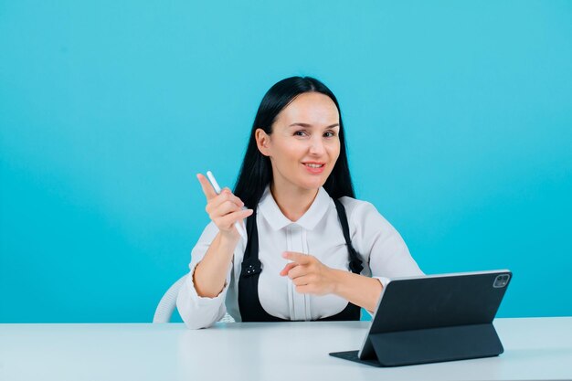 Smiling blogger girl is looking at camera by holding pencil on blue background