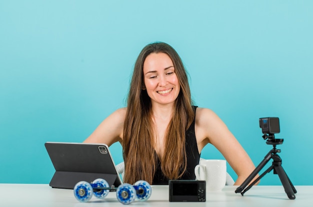 Foto gratuita la ragazza sorridente del blogger sta guardando la sua piccola macchina fotografica su sfondo blu