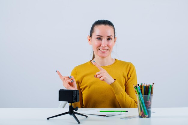 Smiling blogger girl is pointing left with forefingers on white background