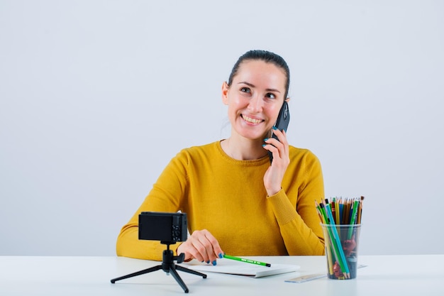 Smiling blogger girl is talking on phone by looking up on white background