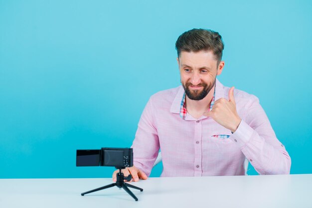 Smiling blogger man is showing perfect gesture by looking at his mini camera on blue background